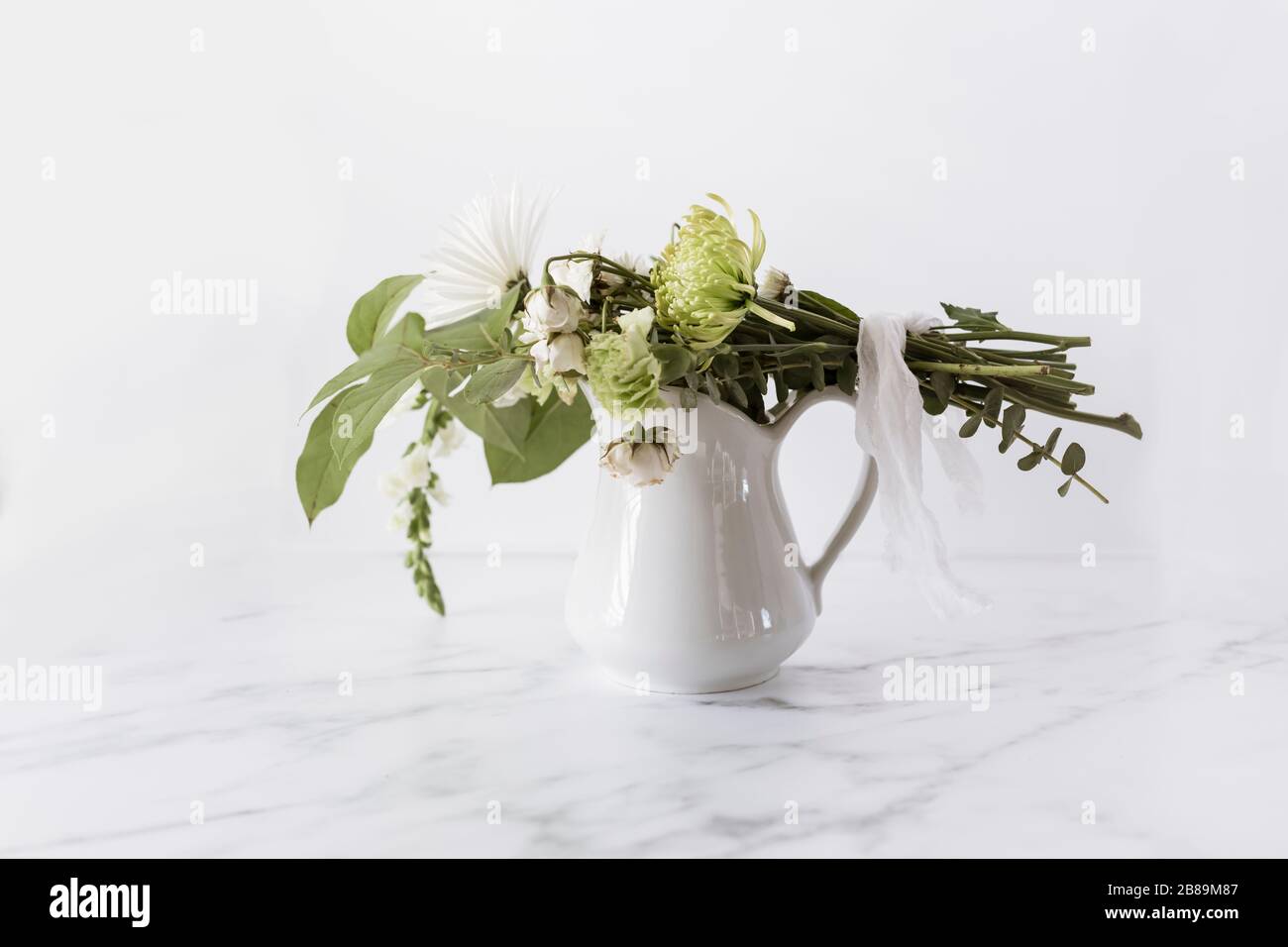 Blumenstrauß mit Leinenband gebunden, der auf weißem Krug liegt Stockfoto