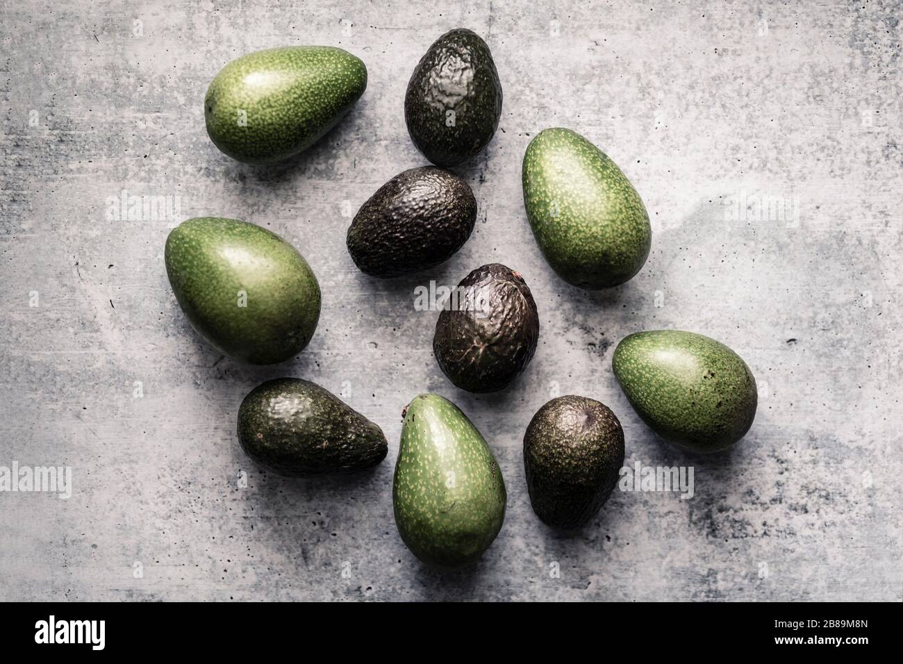 Verschiedene Avocados, die in einer zufälligen Gruppe auf neutralem Hintergrund liegen Stockfoto