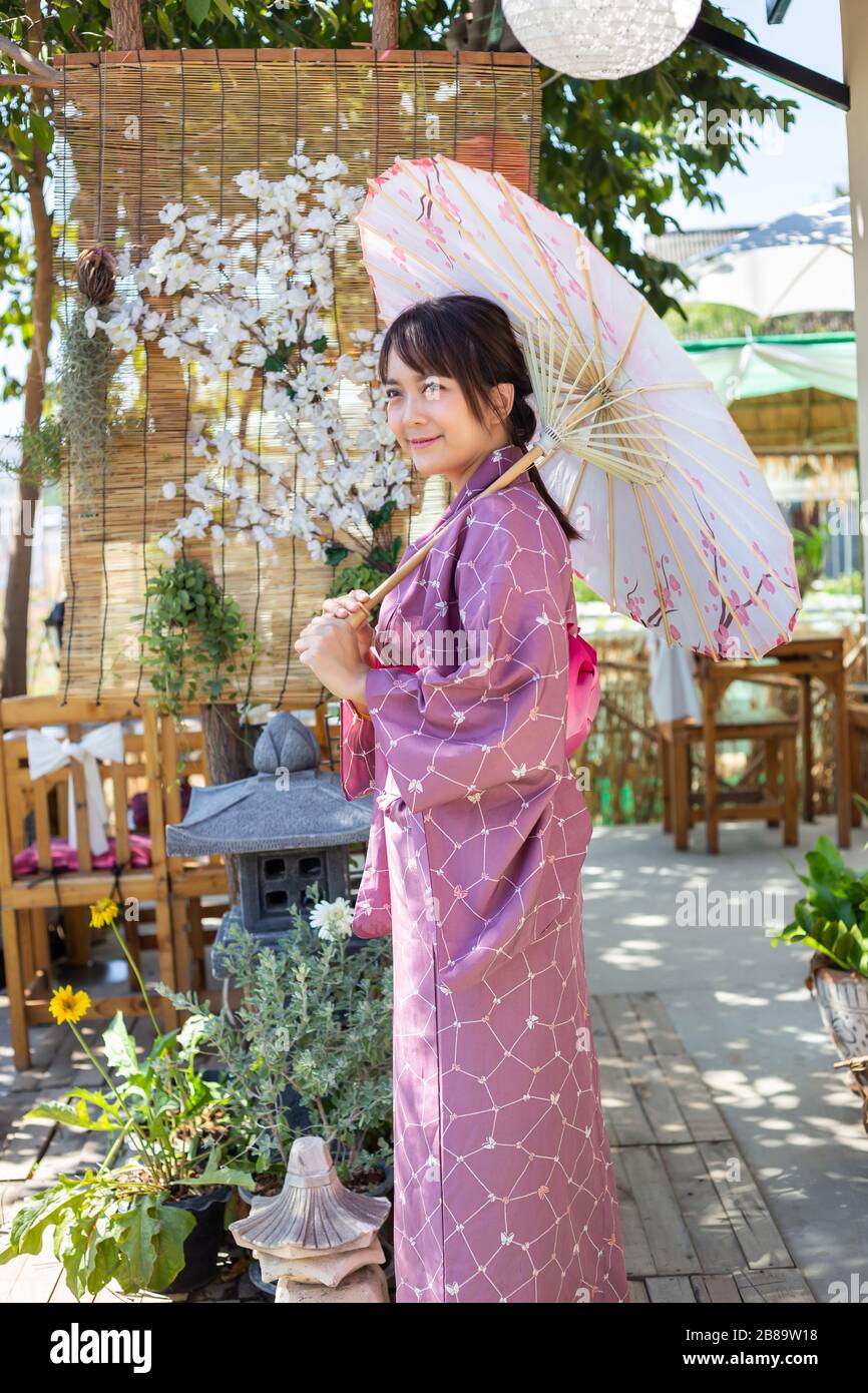 Das Mädchen trägt eine rosafarbene traditionelle Yukata, die das Nationalkleid Japans ist und einen Regenschirm hält Stockfoto