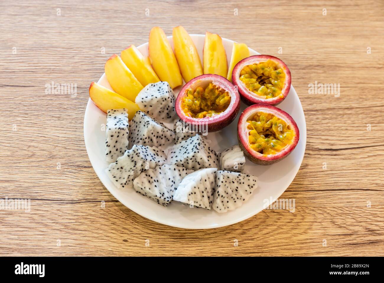 Passionsfrucht, Drachenfrucht, in Scheiben geschnittene Äpfel und schön in einer verzehrfertigen Reisschale auf einem Holztisch angeordnet Stockfoto