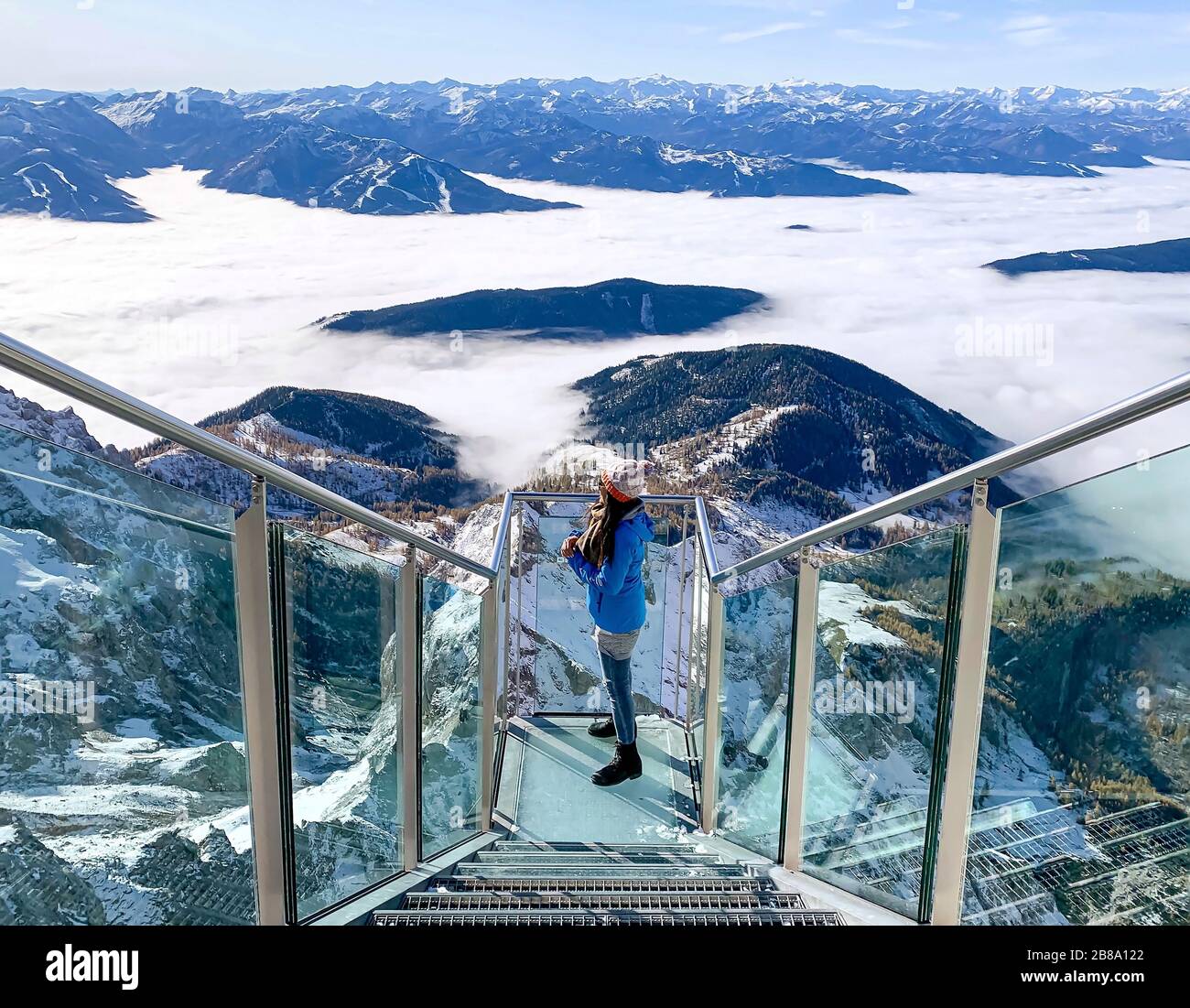 Weibliche Person, die auf einem Skywalk Glass am Dachstein steht und im Winterurlaub den Blick auf die verschneiten Berge in Österreich genießt Stockfoto