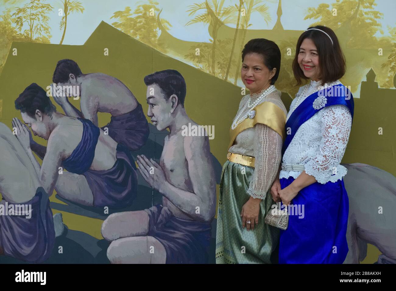 Während der Feierlichkeiten zu Ehren des verstorbenen Königs Bhumipol posieren Frauen in traditioneller Kleidung vor einem Wandbild, das "wai-ing Thais" zeigt; Bangkok, Thailand Stockfoto