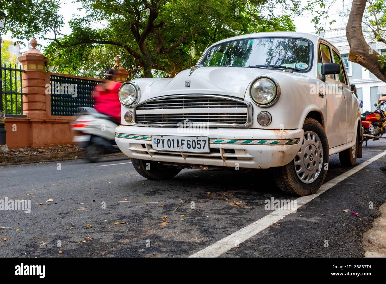 Pondicherry, Indien - 17. März 2018: Alter weißer indischer Wagen (Hindustan Ambassador) und ein Roller, der mit Bewegungsunschärfe vorbeifährt Stockfoto