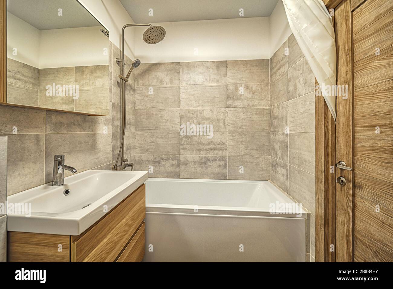Helles, sauberes, Kleines, beigefliestes Badezimmer mit Badewanne und Waschbecken Stockfoto