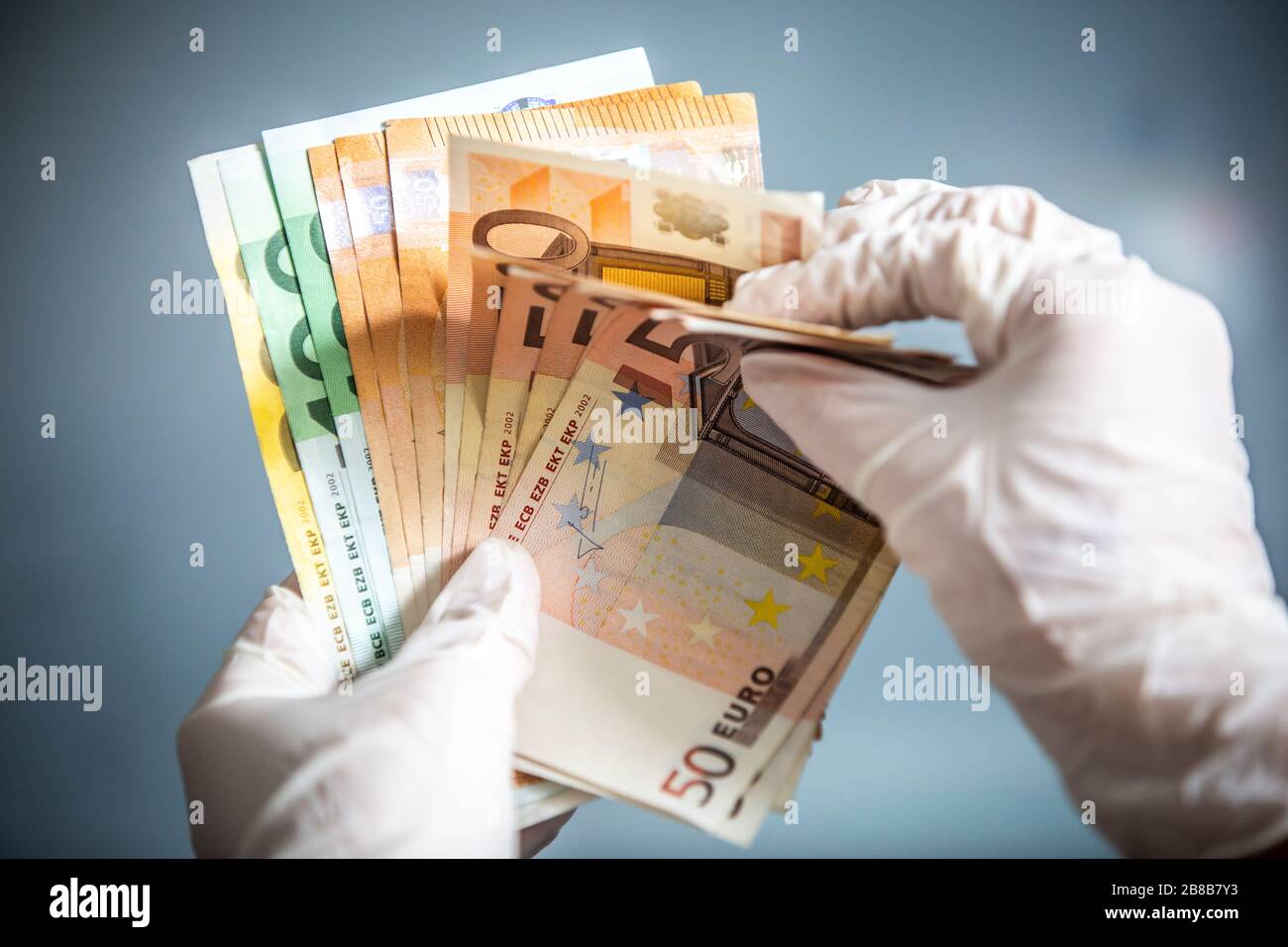 Mann, der Euro-Währungsrechnungen mit Händen hält, die chirurgische Handschuhe tragen, um sich vor Bakterien und Viren zu schützen. Stockfoto
