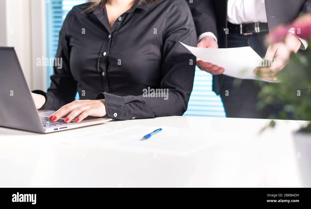Team von Anwälten oder Geschäftsleuten, die zusammenarbeiten. Chef oder Vorgesetzter, der das Papierdokument hält und liest, während der Assistent einen Laptop verwendet. Stockfoto