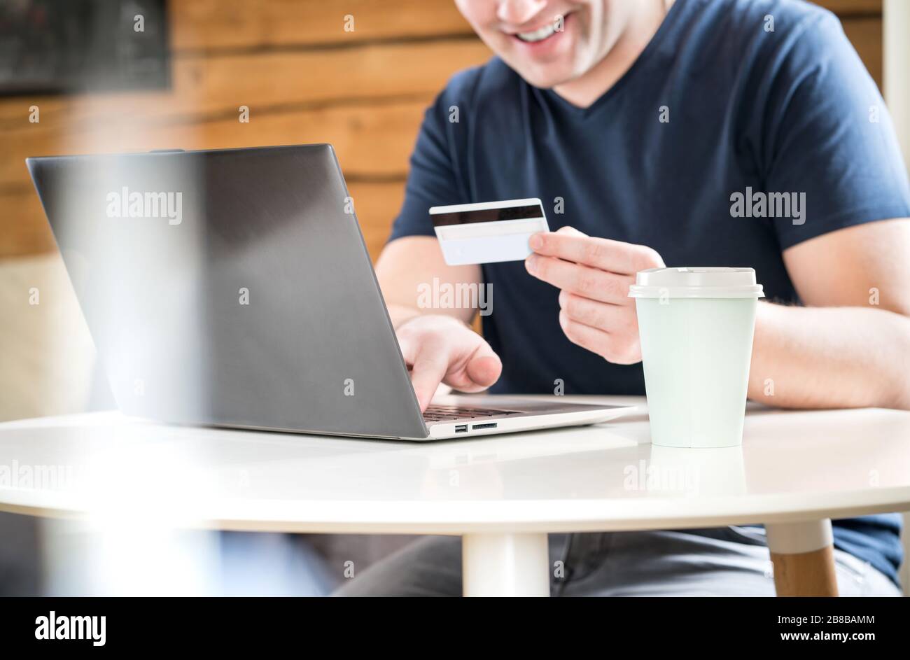 Glücklicher Mann, der mit Kreditkarte bezahlt oder eine Online-Bank mit Laptop verwendet. Fröhlicher und lächelnder Typ, der Informationen oder Zahlen auf den Computer schreibt. Stockfoto