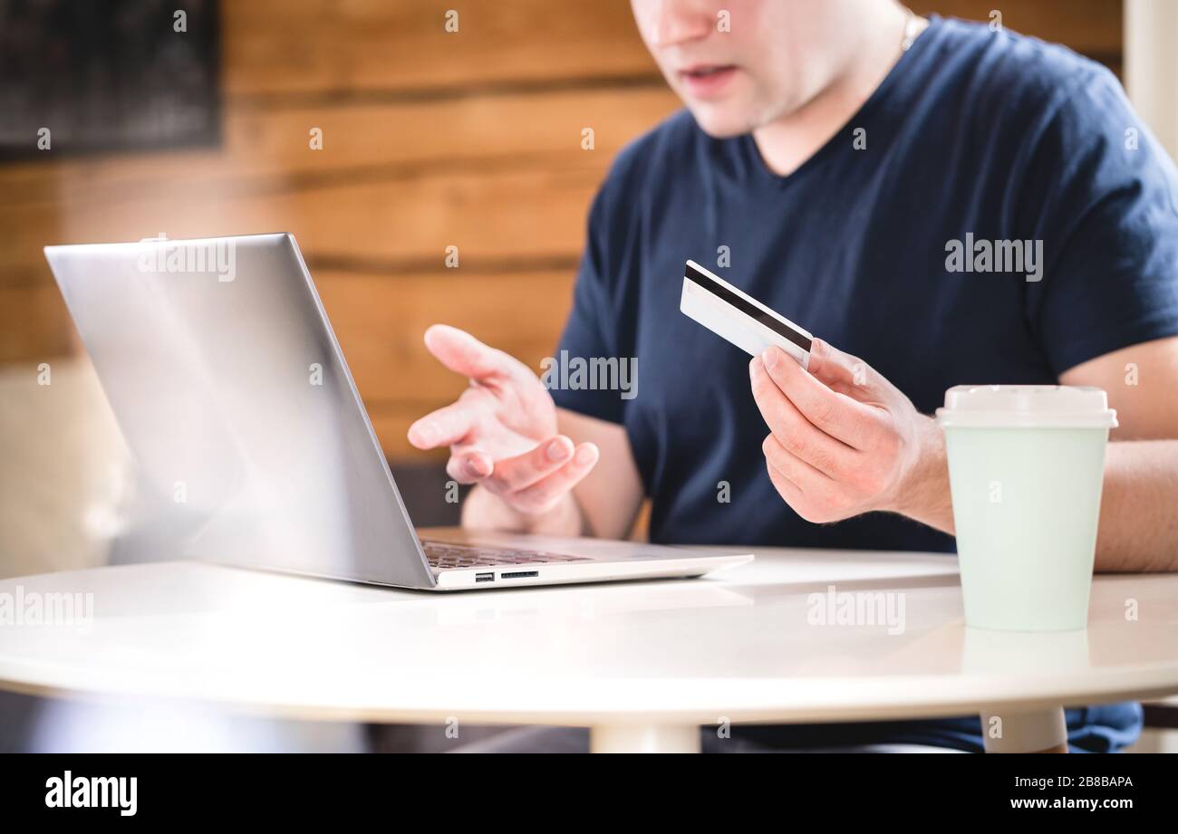 Kreditkartenproblem. Online-Bank funktioniert nicht oder schlechte Internetverbindung. Verwirrter und überraschter Mann, der Bankkarte hält und die Hände streunte. Stockfoto