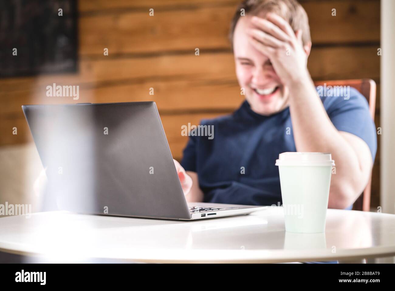 Mann lacht, während er einen Laptop benutzt. Fröhlicher lächelnder Kerl mit Computer im Café, Café oder Zuhause. Lebensfreude, Glück. Lustige Videos ansehen oder streamen. Stockfoto