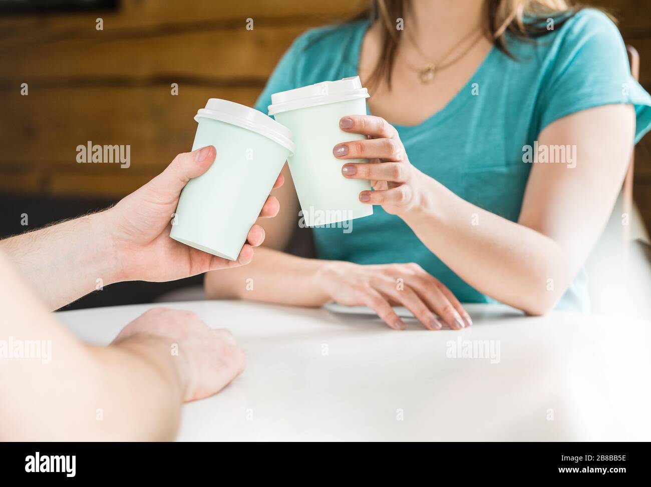 Zwei Freunde oder Paare halten Kaffeetassen zusammen und jubeln im Café. Vereinbarung, Besprechung oder Feier. Mann und Frau kleben. Prost! Stockfoto