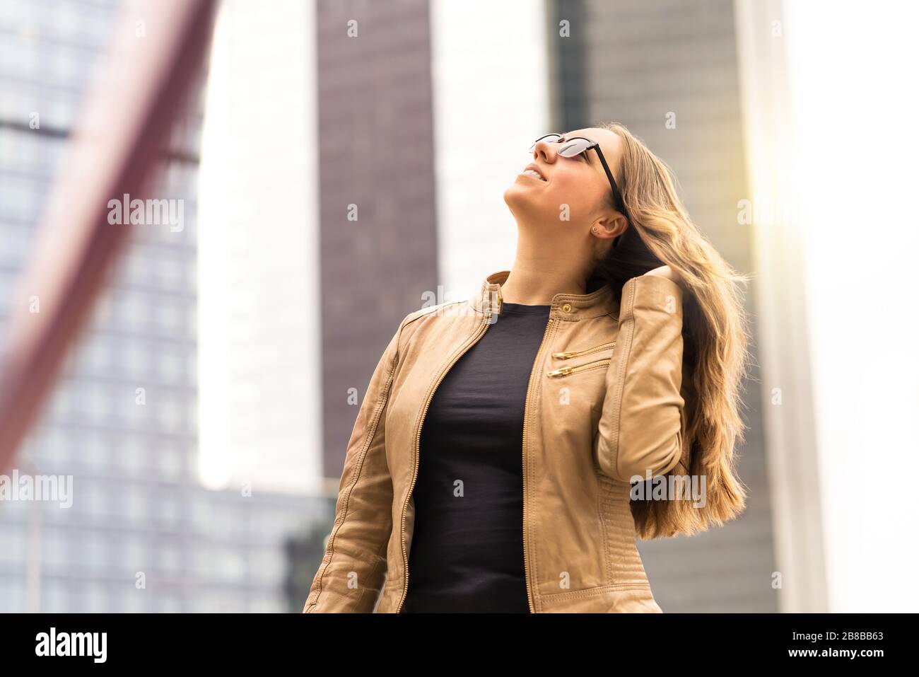 Selbstbewusste Brunette-Frau, die in der Stadt spazieren geht. Starke Dame, die bei Sonnenuntergang braune Haare feilte. Urbaner modischer Lebensstil. Stockfoto