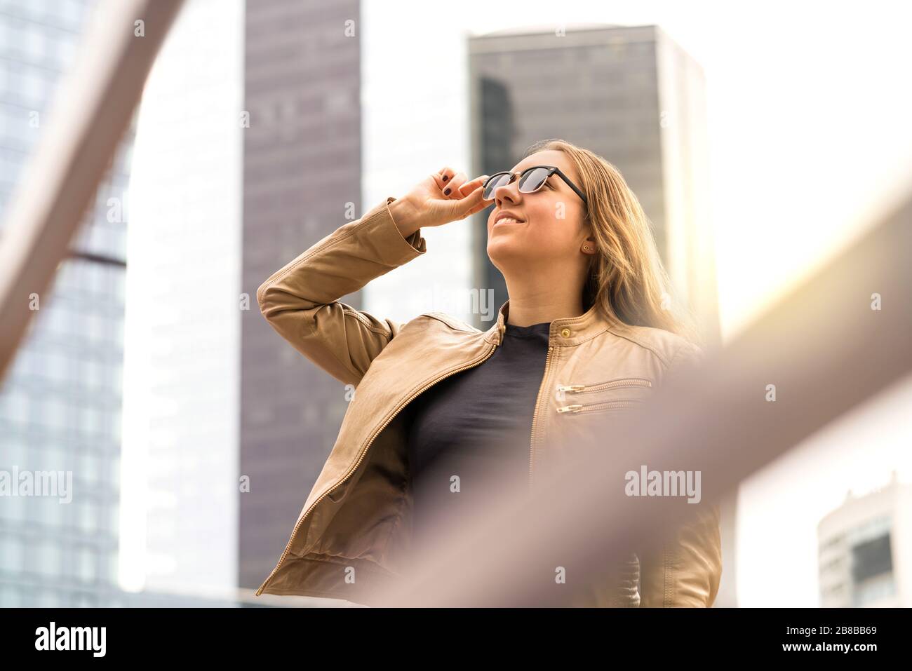 Erfolgreiche junge Frau in der Großstadt mit Hochhäusern und Wolkenkratzern. Elegante und selbstbewusste Dame mit Sonnenbrille. Stockfoto