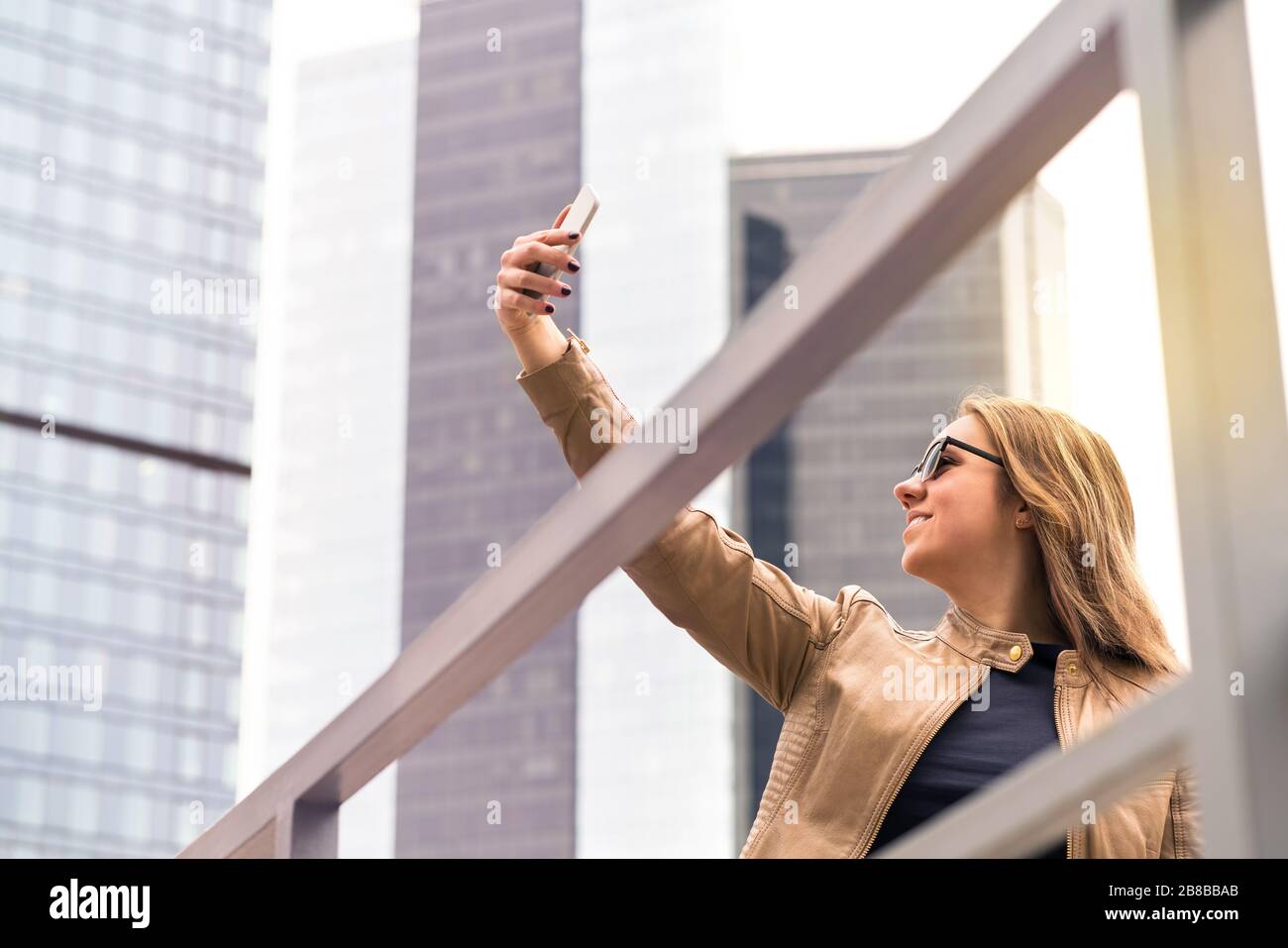 Junge glückliche Frau, die selfie auf der Straße der Stadt mitnimmt. Lächelnde Dame fotografiert mit Smartphone-Kamera. Handyfotografie. Stockfoto