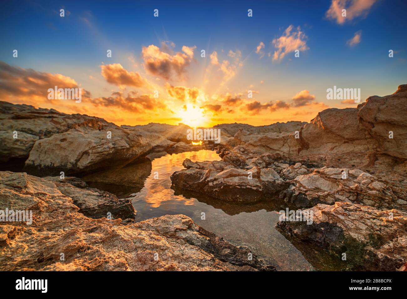 Schöner farbenfroher Sonnenuntergang am Meer auf Zypern mit dramatischen Wolken und Felsbrocken. Reflexionen im Wasser. Beauty-Welt Natur im Freien Reise-Hintergrund Stockfoto