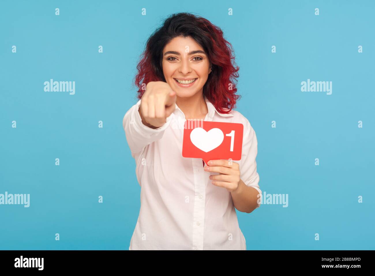 Du drückst "gefällt mir"-Taste in sozialen Medien! Portrait eines hübschen Mädchens mit fantasievollen roten Haaren, die Herzsymbol halten und auf die Kamera zeigen, und empfehlen, einem zu folgen Stockfoto