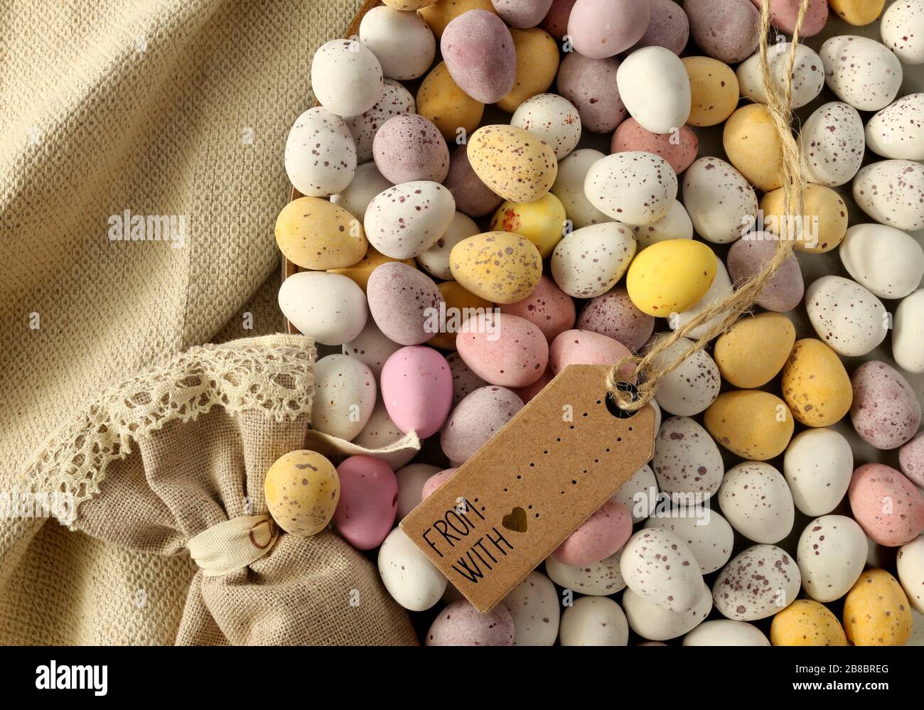 Mehrere farbenfrohe Ostereier aus Schokolade auf dem runden Teller, Geschenkbeutel aus Leinwand, Frühlings-Blumenstrauß. Flatlay, Ansicht nach oben. Ostern, Frühlingssymbol Stockfoto