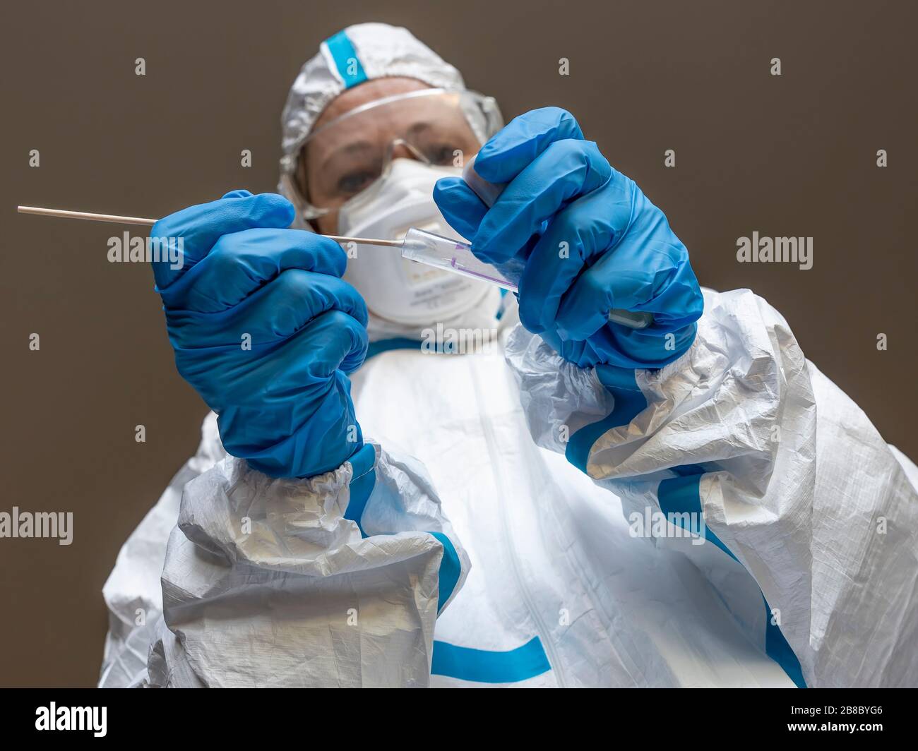Eine Frau, Labortechnikerin, die mit einem weißen Schutzhülle bedeckt ist, macht einen Testabstrich, um auf eine mögliche Ansteckung von Coronavirus Covid-19 zu prüfen Stockfoto