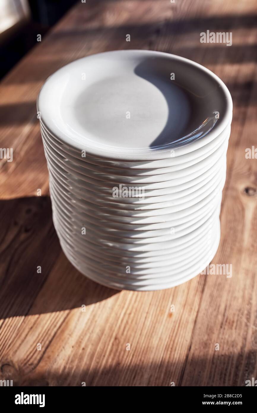 Stapel weißer Teller auf dem Holztisch eines Restaurants oder Cafés unter natürlichem Sonnenlicht am Nachmittag. Stockfoto