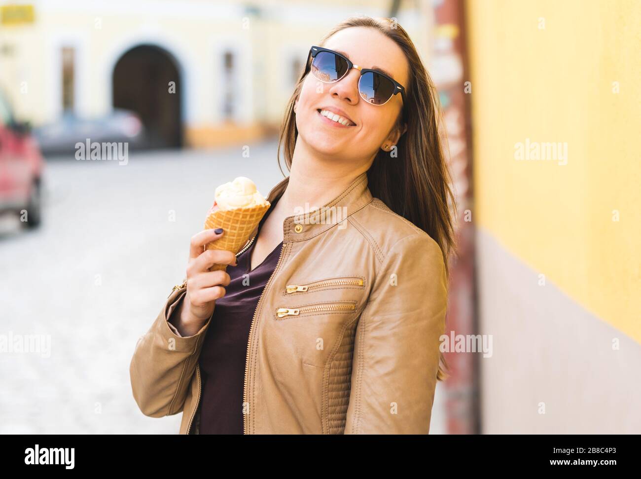 Aufgeregte und energische Frau, die Eiskegel in der Stadt hält. Fröhlicher stilvoller Mensch, der süße Leckerbissen in der städtischen Straße isst. Stockfoto