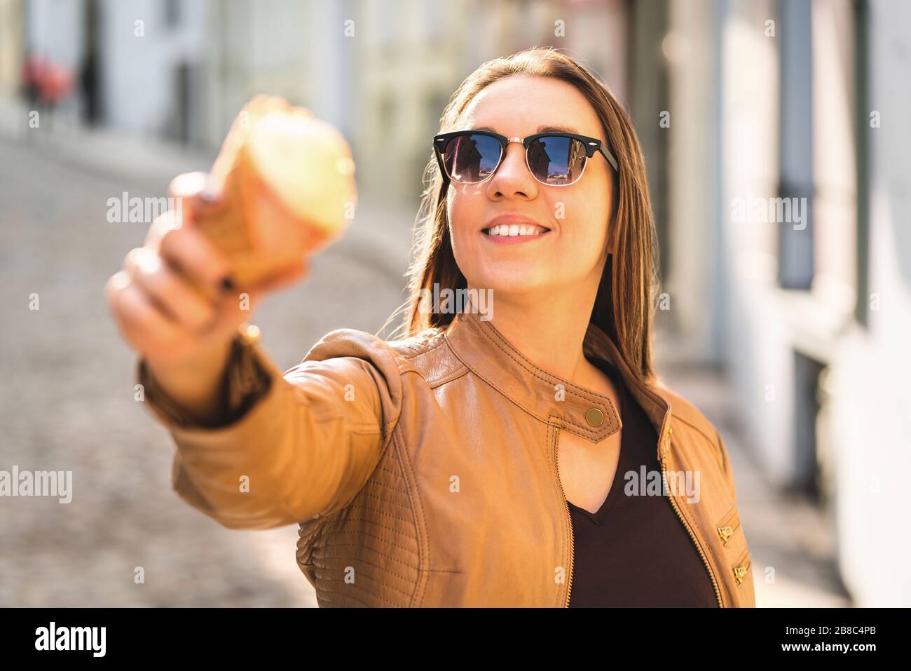 Lächelnde Frau, die einen Eiskegel auf die Kamera zeigt und zeigt. Person goofing und durcheinander mit süßem Dessert in der Stadt. Stockfoto