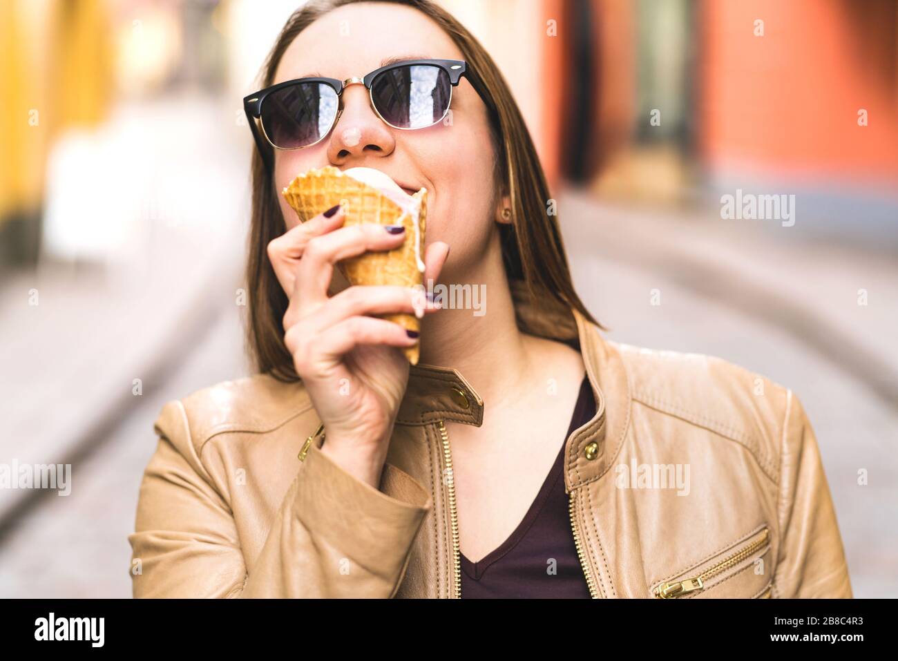 Frau, die unordentliche schmelzende Eiscreme isst und lacht. Fröhliches lächelndes Mädchen, das Spaß hat und ein tropfendes Dessert in der Straße der Stadt hält. Lustiger urbaner Lebensstil. Stockfoto