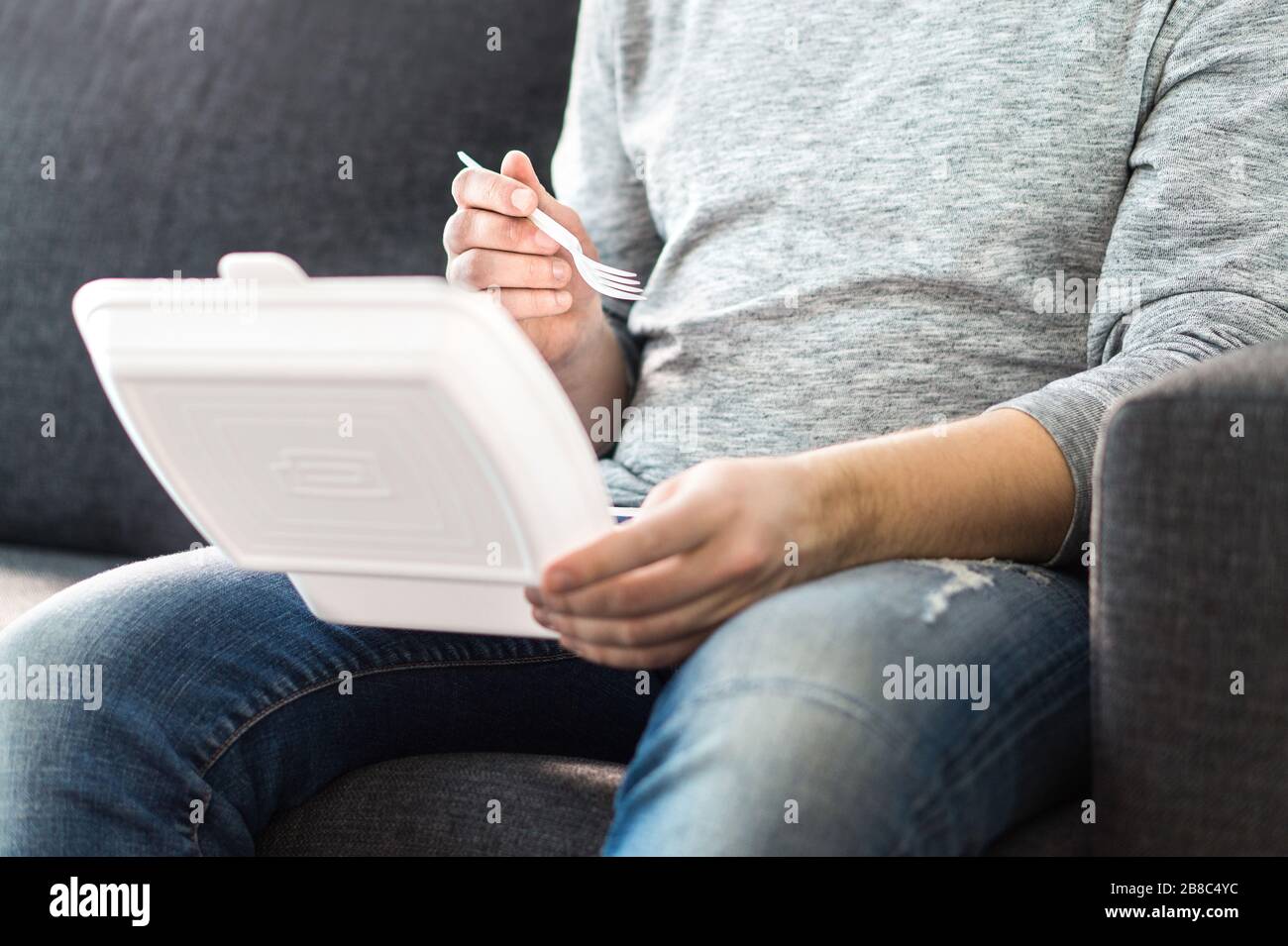 Kerl, der Essen wegnimmt. Mann, der Kebab oder chinesisch aus Fast-Food-Box genießt. Sie sitzen zu Hause auf der Couch und haben ein Essen zum Mitnehmen. Stockfoto