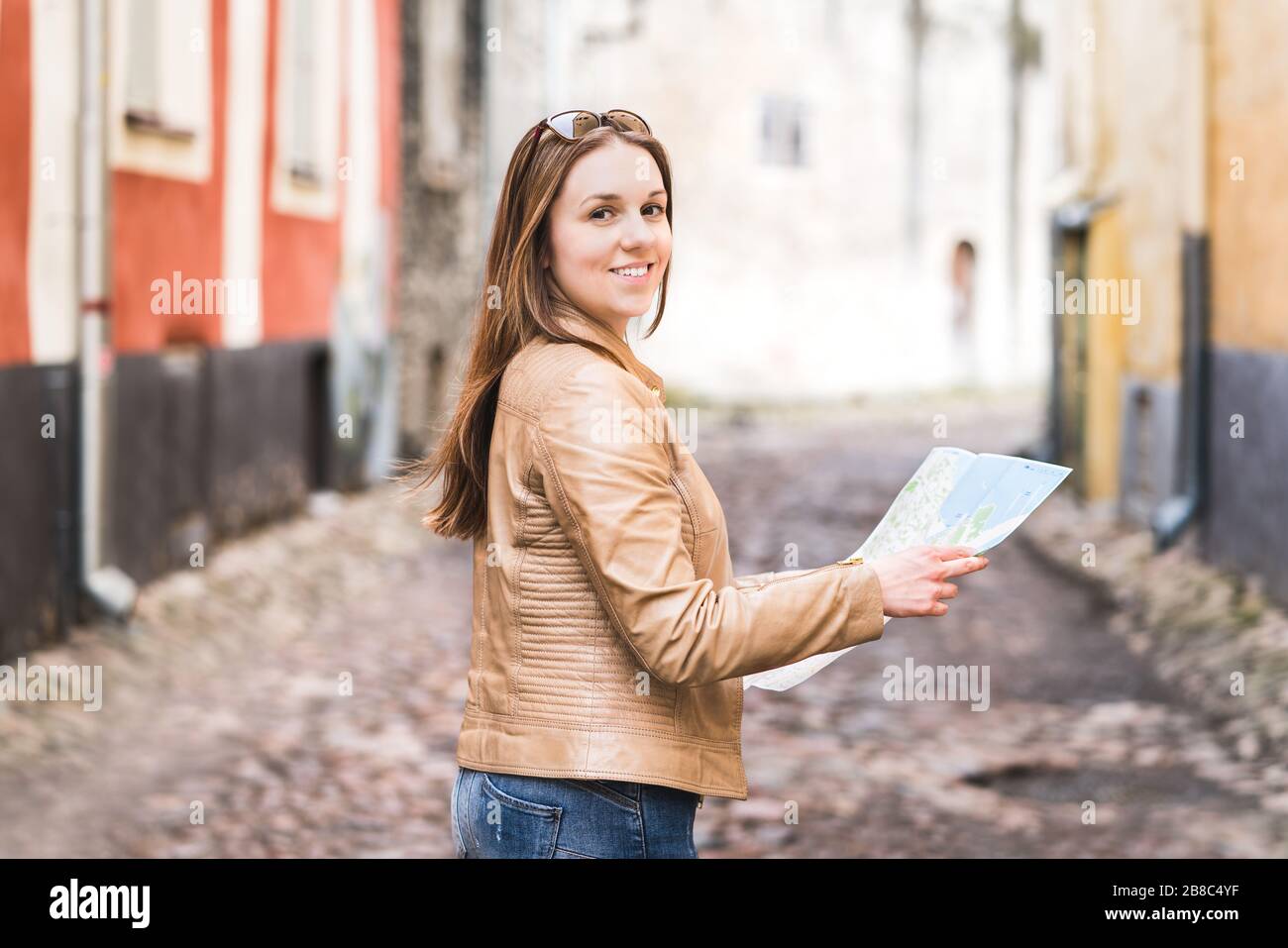 Frau mit Karte direkt zur Kamera. Fröhliche weibliche Reisende in der Stadt oder in der Altstadt posieren. Porträt einer lächelnden Person im Urlaub. Stockfoto