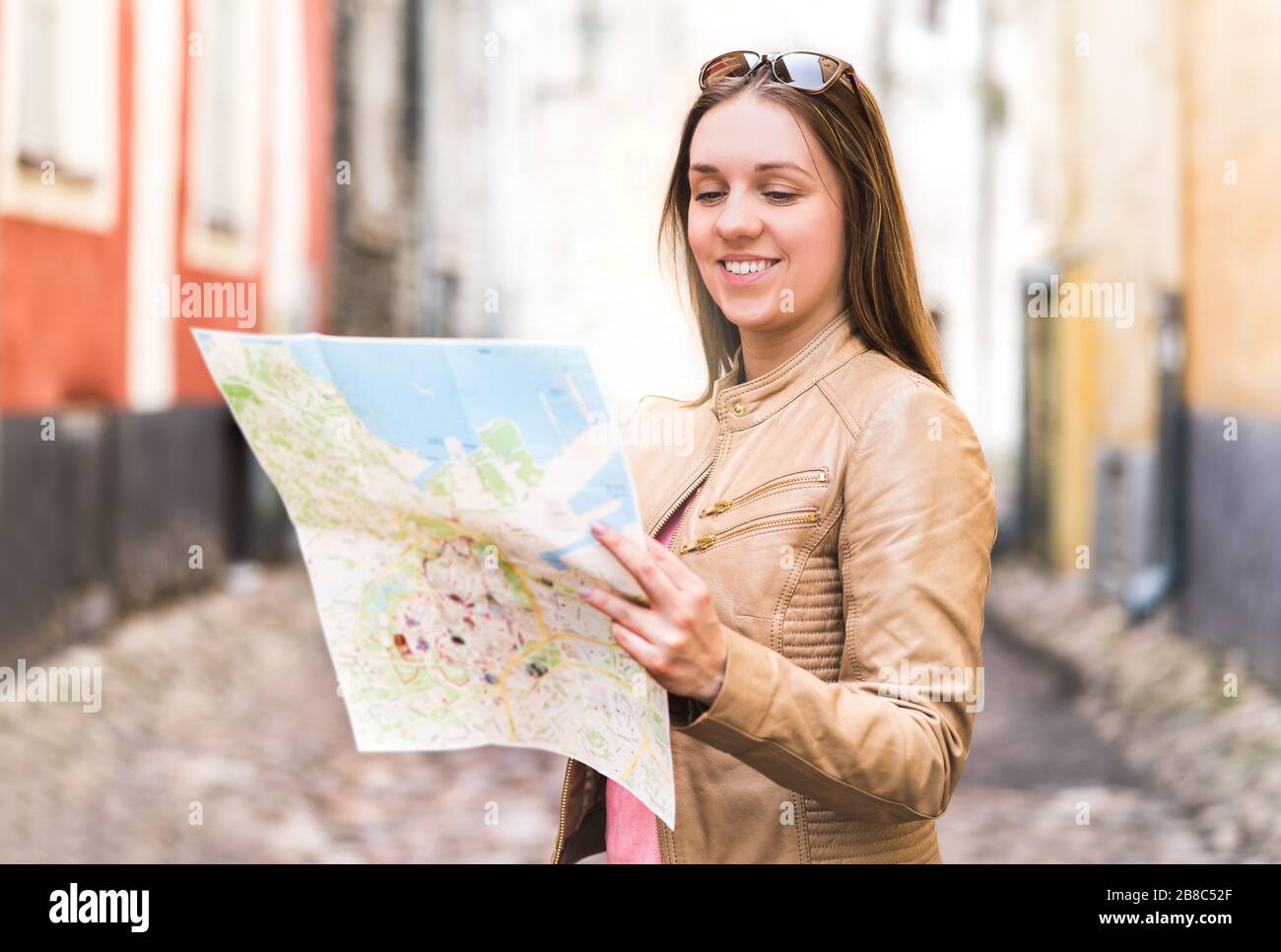 Fröhliche junge Frau liest Karte. Lächelnder Reisender bei der Navigation und Planung von Besichtigungstouren in der Stadt. Person im Urlaub in der Altstadt. Stockfoto