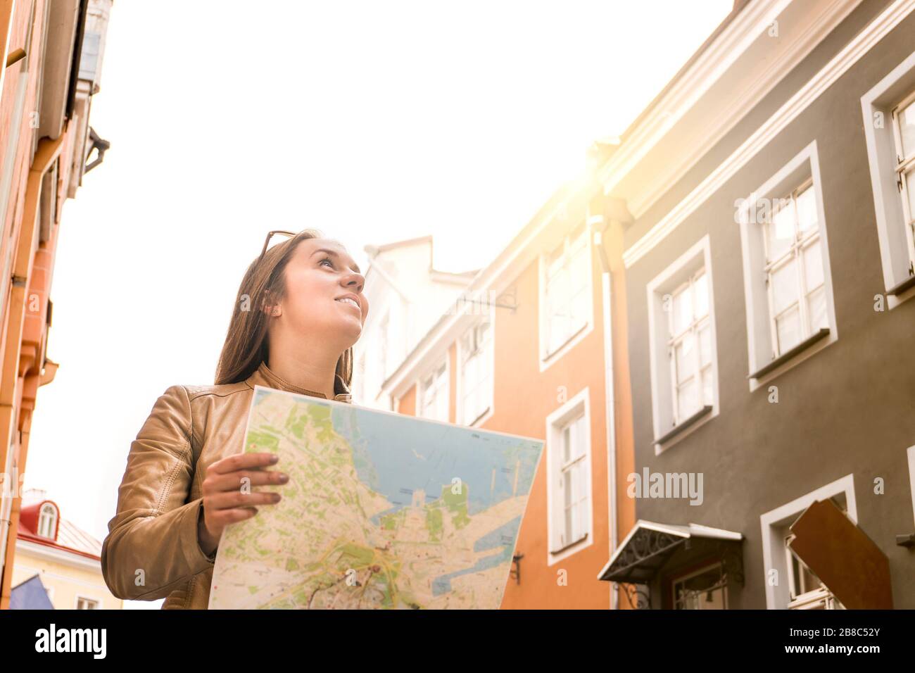 Frau, die in der Stadt mit Karte spazieren geht. Reise-, Wanderlust- und Sightseeing-Konzept. Fröhlicher lächelnder Tourist in der Stadtstraße mit alten Gebäuden. Stockfoto