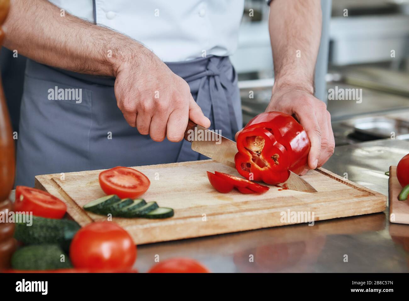Koch in Uniform macht seinen Job. Er hackt Gemüse für sein unverkennbares Gericht. Kochkonzept. Zugeschnittenes Bild Stockfoto
