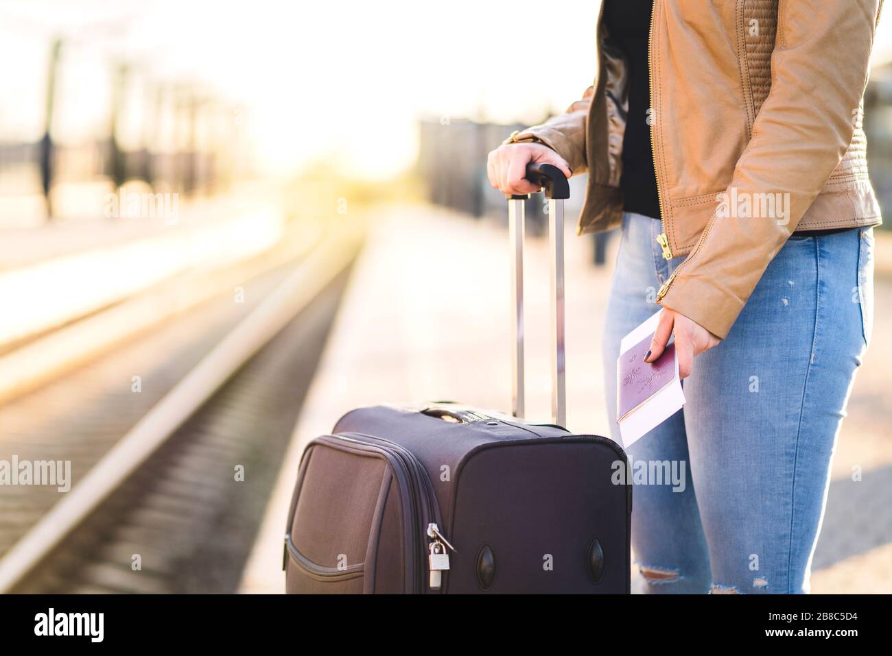 Frau wartet mit Koffer und Gepäck auf Zug. Dame, die Fahrkarte und Reisepass in der Hand in der Plattform hält. Tracks im Hintergrund. Stockfoto