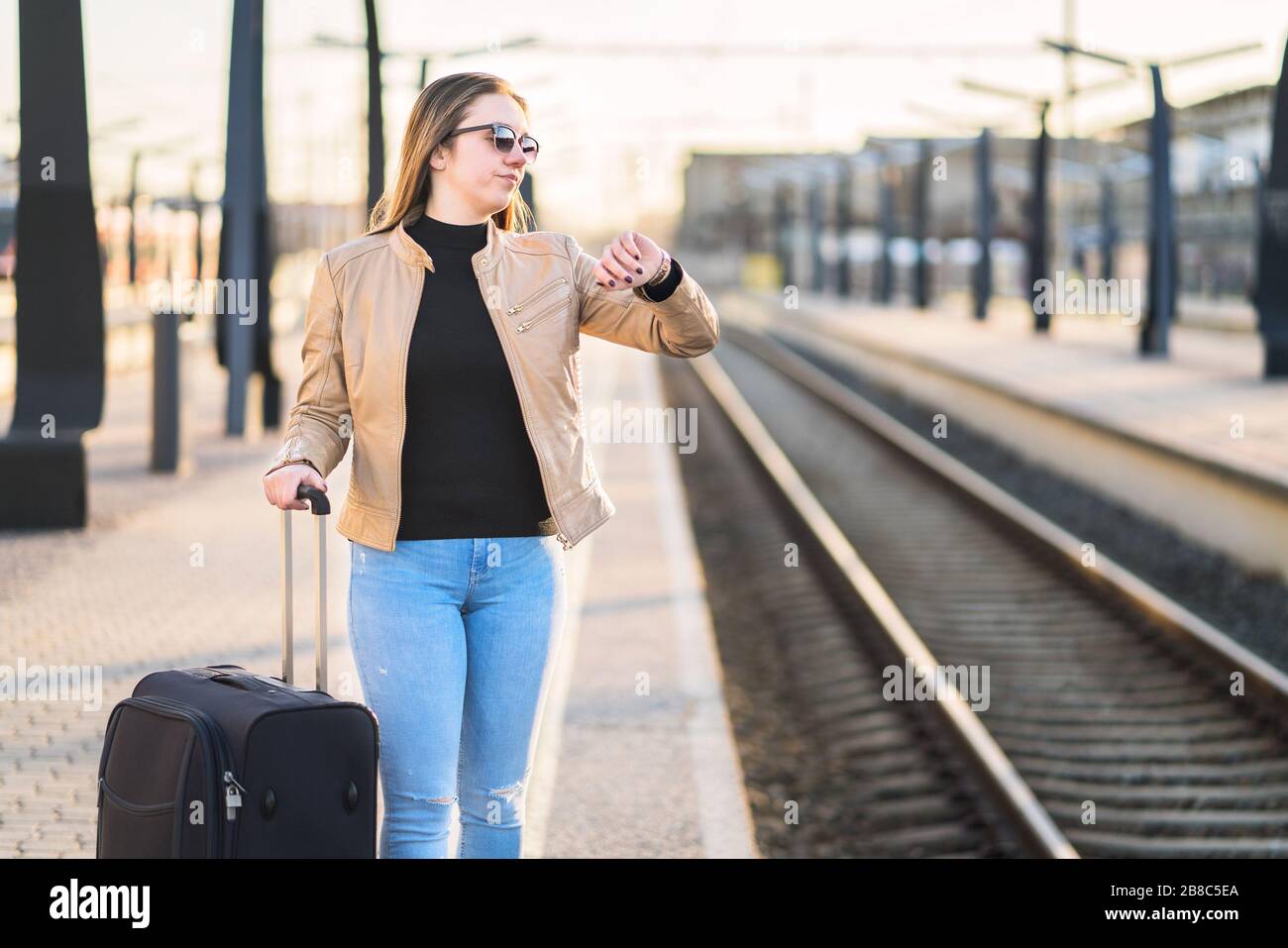 Unglückliche und frustrierte Frau, die die Zeit betrachtet und am Bahnhof zuschaut. Verärgerter Passagier auf Bahnsteig. Stockfoto