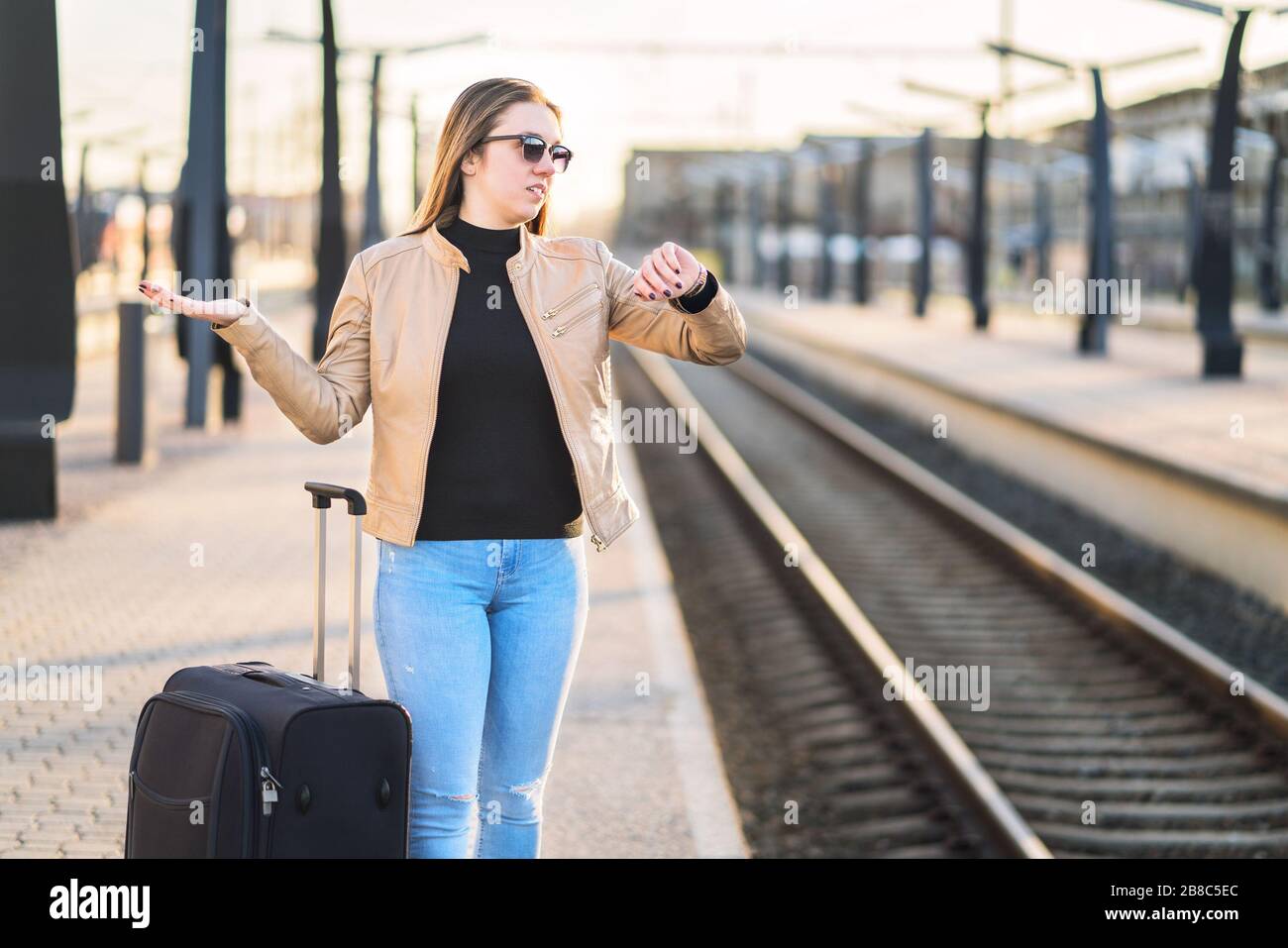 Verspätete, verspätete, stornierte oder verfahrene Züge. Verwirrte Frau, die sich die Zeit ansieht und zuschaut, während sie auf der Plattform wartet. Stockfoto