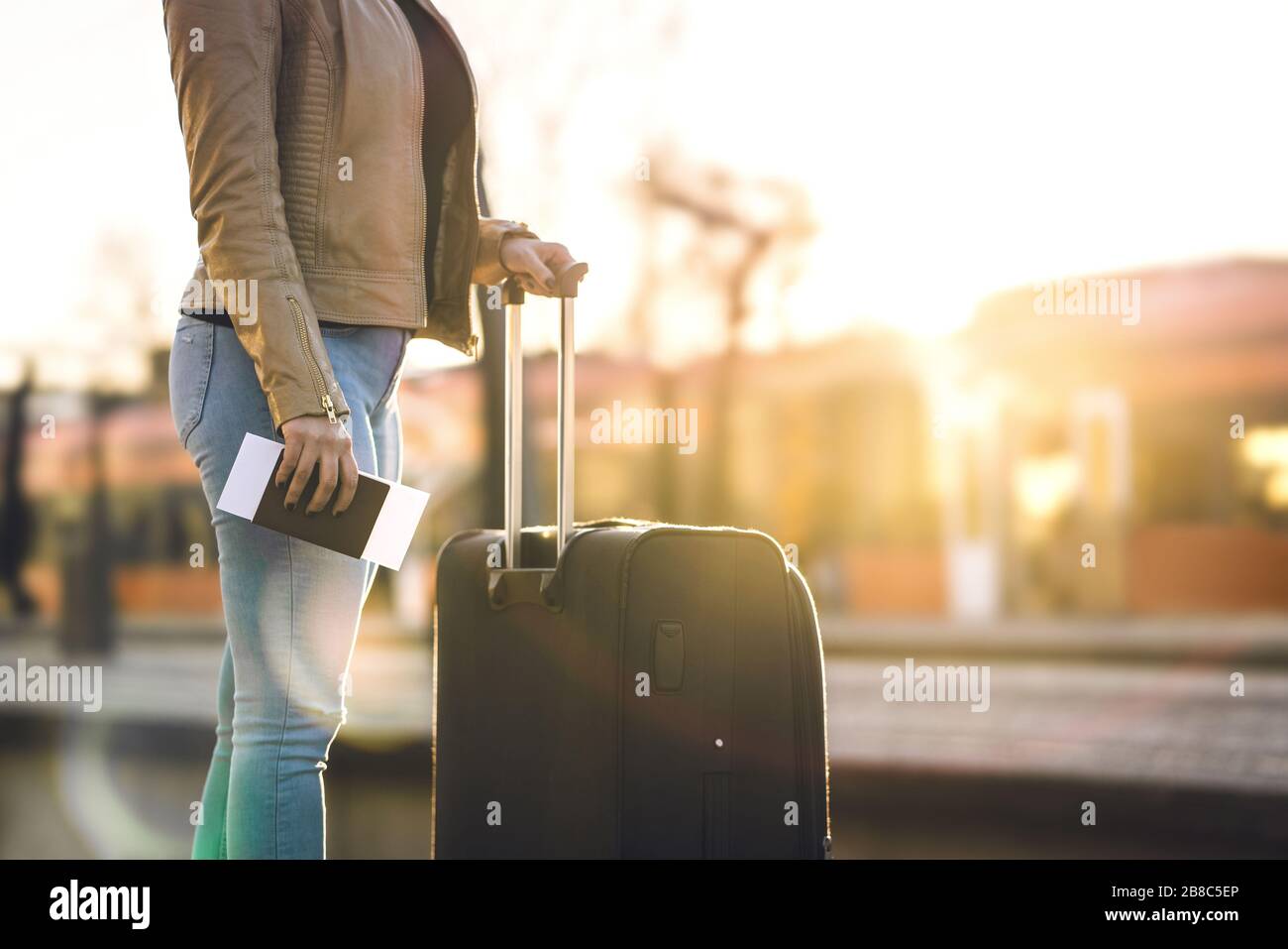 Bahnhof bei Sonnenuntergang. Frau, die in der Plattform steht und Fahrkarte und Reisepass in der Hand hält. Person mit Koffer und Gepäck. Stockfoto