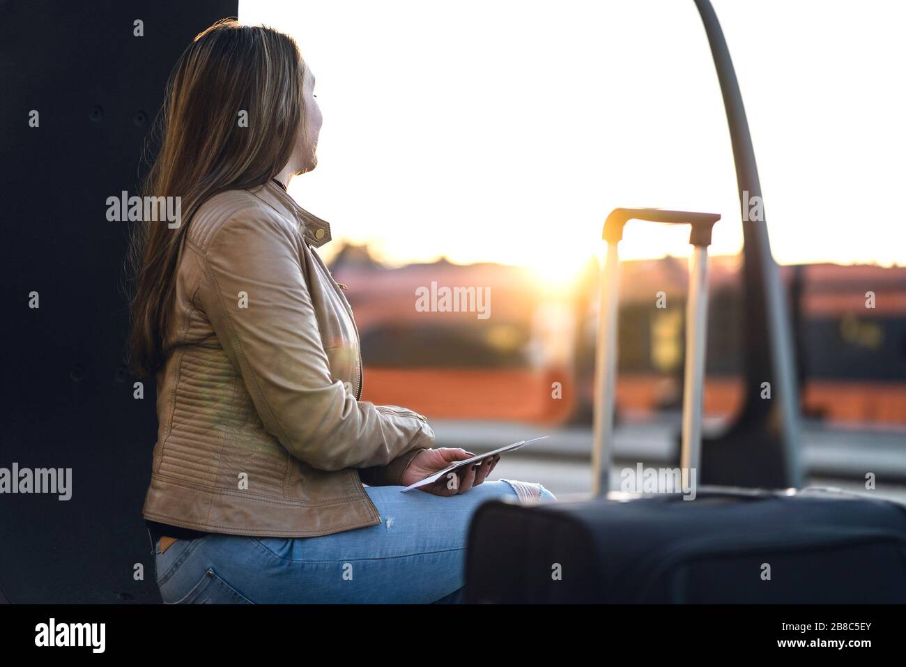 Dame sitzt und wartet im Bahnhof auf den Zug. Frau in Plattform bei Sonnenuntergang mit Koffer, Ticket und Pass. Stockfoto