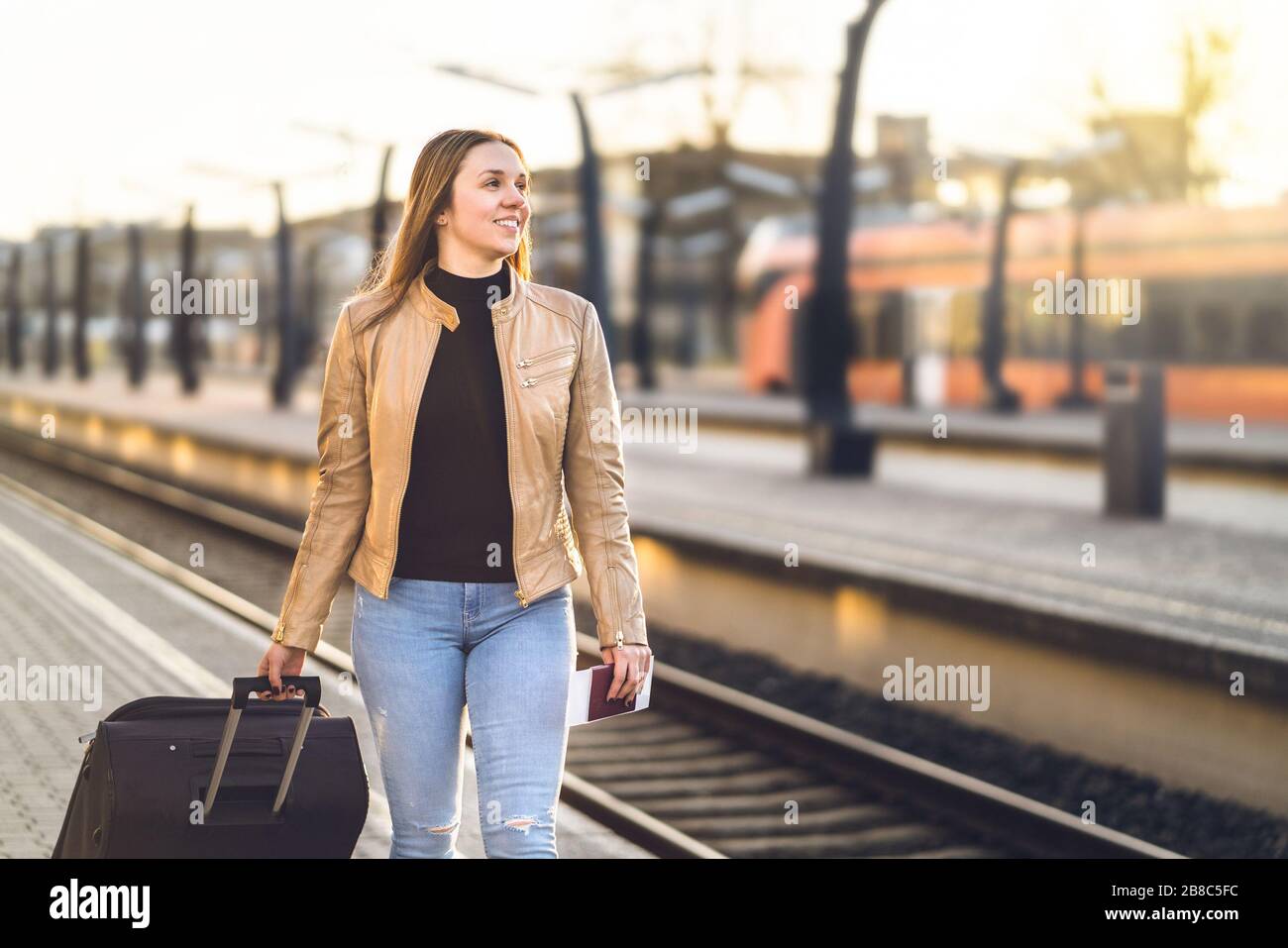 Dame zieht Koffer und Gepäck im Bahnhof. Frau, die auf dem Bahnsteig spazieren geht und Fahrkarte und Reisepass vorhält. Glückliche weibliche Reisende. Stockfoto