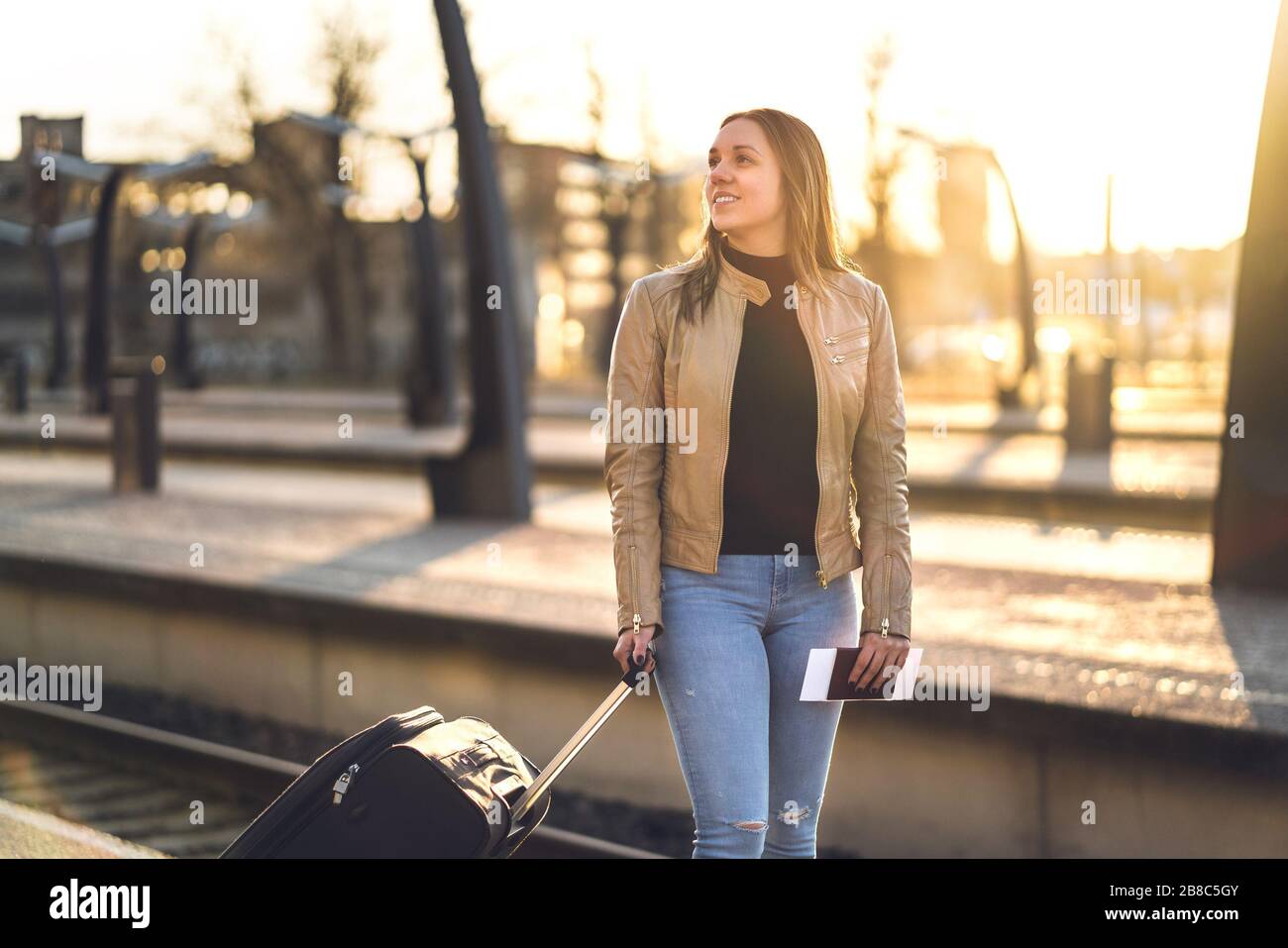 Reisender, die bei Sonnenuntergang auf dem Bahnsteig stehen. Lächelnde Frau, die mit Koffer, Gepäck und Gepäck am Bahnhof wartet. Reise-Lifestyle. Stockfoto