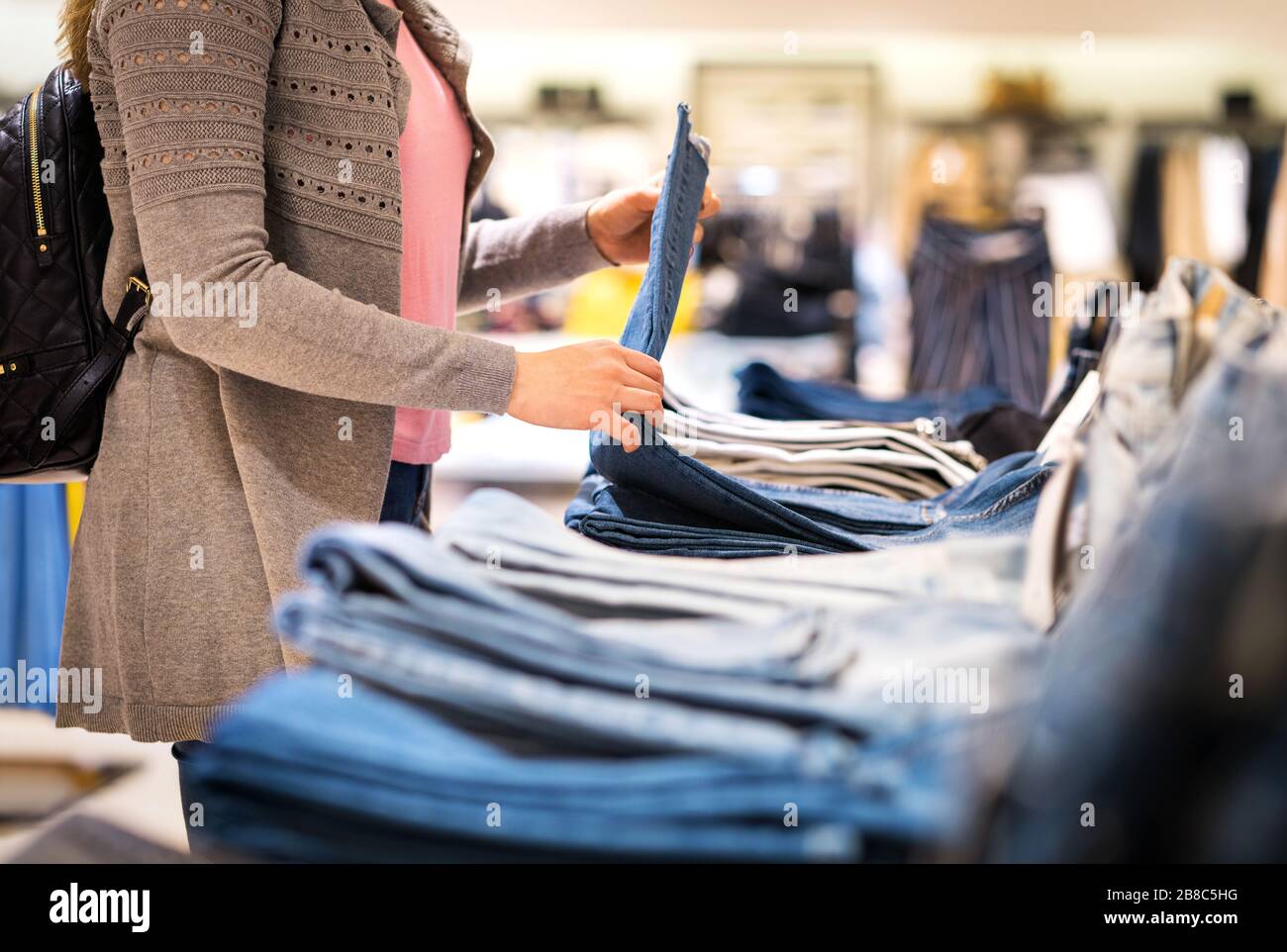 Frau kauft Jeans im Modegeschäft. Weibliche Kunden halten Hosen und schauen sich Stoff und Material an. Stockfoto