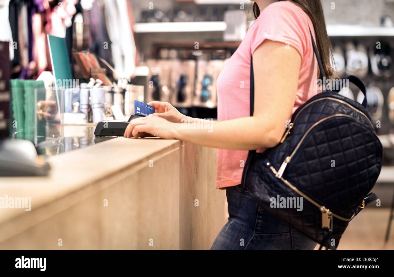 Frau an der Kasse im Modegeschäft, die mit Kreditkarte bezahlt. Kunde verwendet Zahlungsterminalmaschine. An der Theke stehen. Kaufen und Einkaufen. Stockfoto