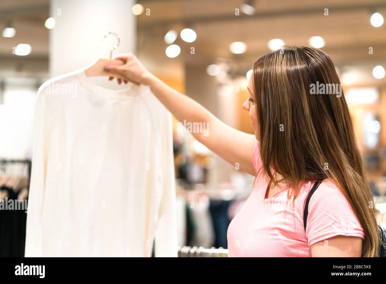 Frau hält Bluse im Kleiderbügel im Modegeschäft. Einkaufen nach Pullover oder Hemd. Zufriedene Kunden und Käufer auf der Suche nach neuer Kleidung. Stockfoto