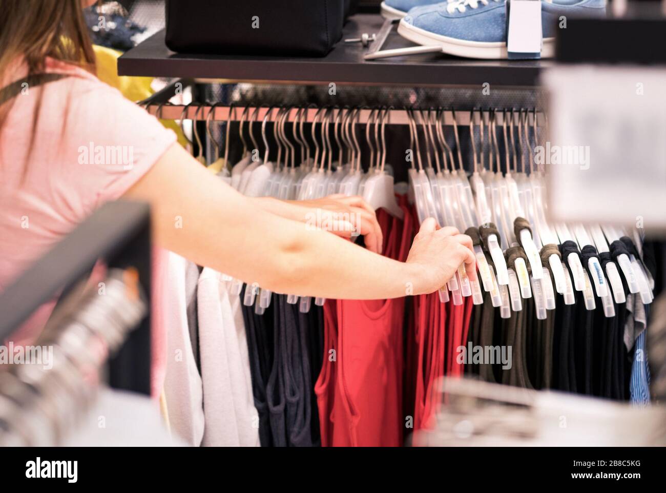 Frau, die im Modehaus Kleidung in einem Regal betrachtet. Einkäufe von weiblichen Kunden. Verkauf und Sonderangebote in der Modeboutique. Nahaufnahme der Hände. Stockfoto