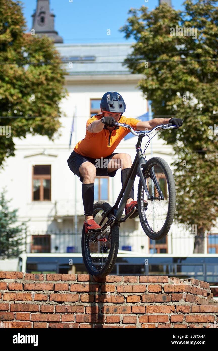 Seitenansicht eines Athleten, der ein Mountainbike-Rad in den Händen hält. Der junge Mann in der Sportkleidung setzte sich ab und sprang. Konzept, auf einem Fahrrad zu stehen. Stockfoto