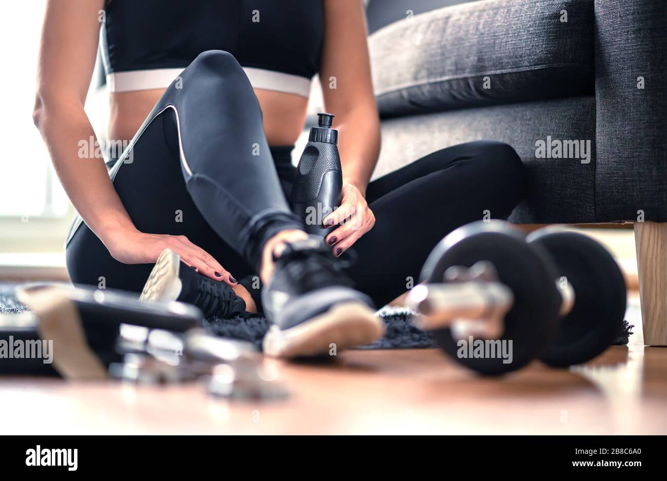 Heimtraining, Krafttraining und Fitness-Trainingskonzept. Frau in Sportswear sitzt im Wohnzimmer mit Fitnessgeräten und Hanteln. Stockfoto