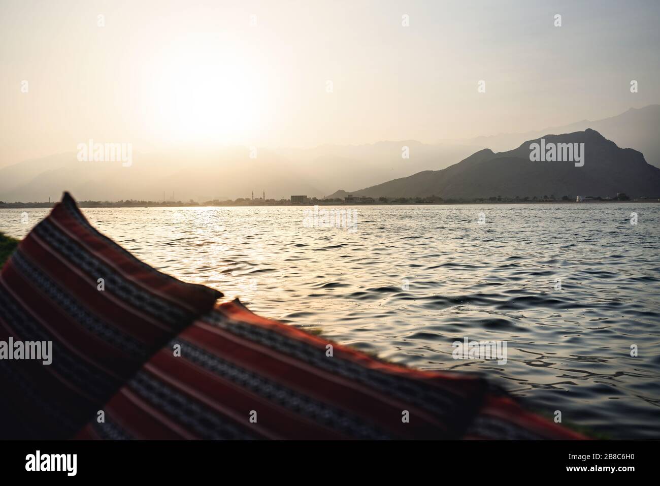 Dhow Bootstour auf der Musandam-Halbinsel in Oman bei Sonnenuntergang. Blick vom Touristenschiff auf die Berge und die traditionelle omanische Stadt mit Moscheen. Stockfoto