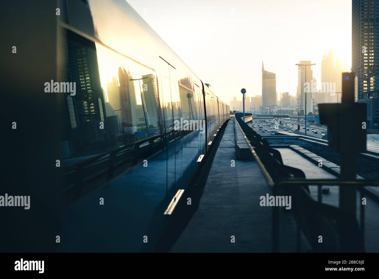 U-Bahn und U-Bahn in der Stadt. Futuristische moderne öffentliche Verkehrsmittel. Dubai Eisenbahnsystem bei Sonnenuntergang mit Wolkenkratzer-Gebäuden und Autoverkehr. Stockfoto