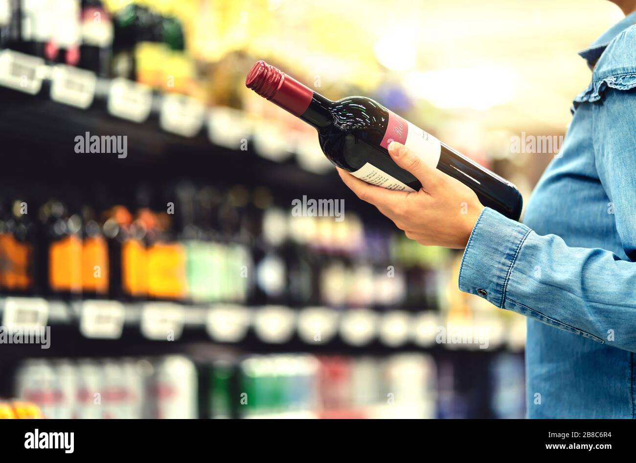 Alkoholregal im Spirituosenladen oder im Supermarkt. Frau kauft eine Flasche Rotwein und schaut im Geschäft auf alkoholische Getränke. Stockfoto