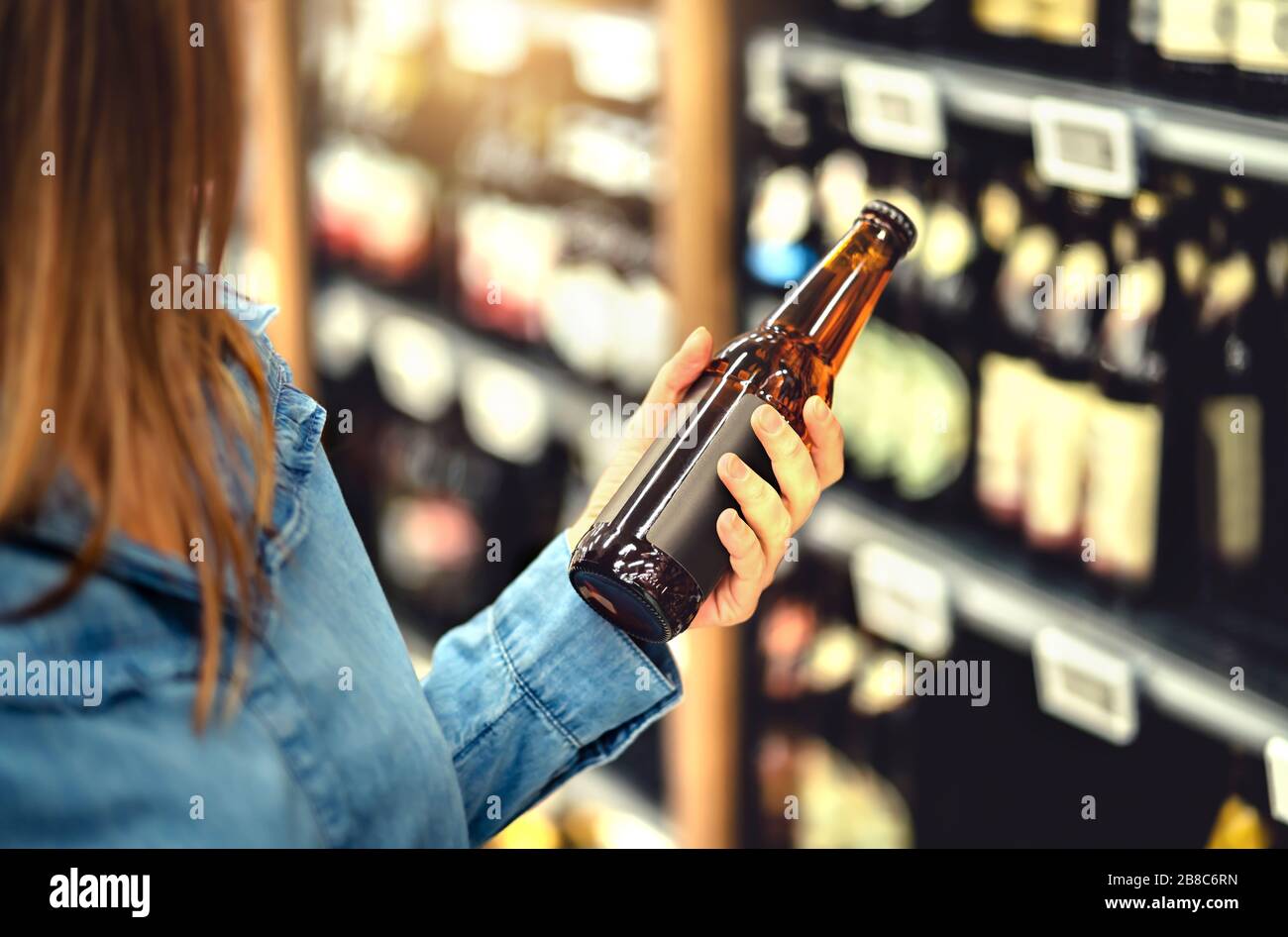 Kunde kauft Bier im Spirituosenladen. Lagerbier, Handwerk oder Weizenbier. IPA oder blasses Ale. Frau im Alkoholregal. Getränkekabinken und Gang im Supermarkt. Stockfoto