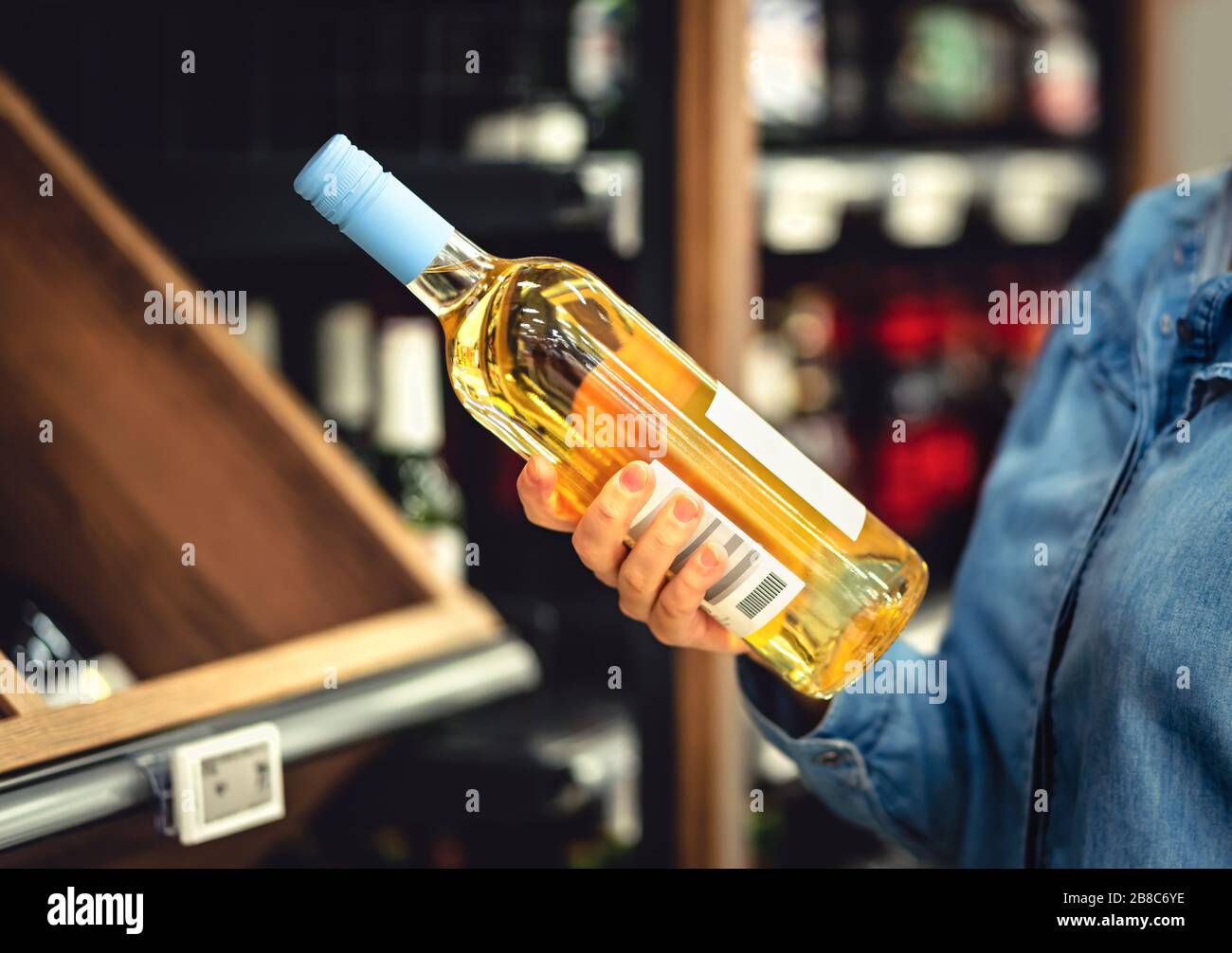 Weißweinflasche in der Hand im Spirituosenladen. Kunde kauft Alkohol. Frau, die die richtige Flasche chardonnay oder Riesling wählt. Alkoholische Getränke. Stockfoto