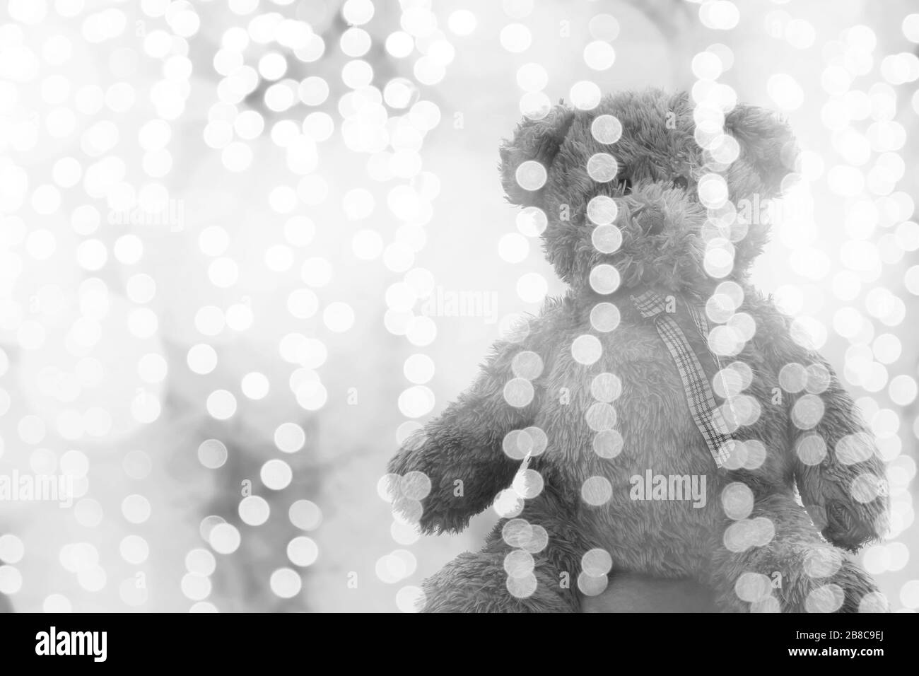 Teddybärpuppe in der Beleuchtung bokeh silberhell für Weihnachten oder fröhlicher Neujahrshintergrund, Bär einsam im glitzernden grauweißen Hintergrund sitzend Stockfoto