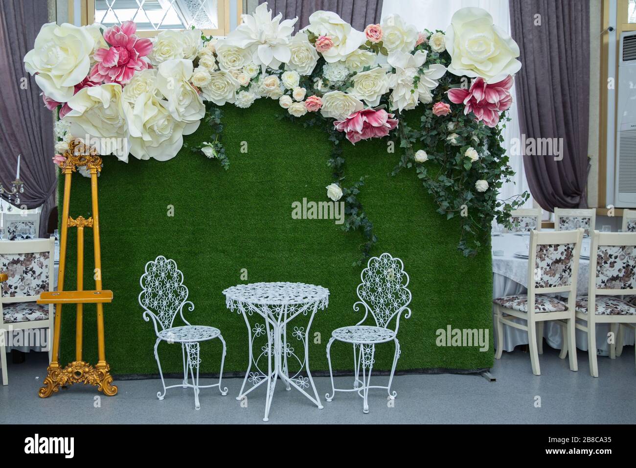 Grüner Hintergrund, weißer runder Tisch, weißer Stuhl, große weiße Blume. Henna und Engagement Dekoration Henna Bühnenparty. Stockfoto